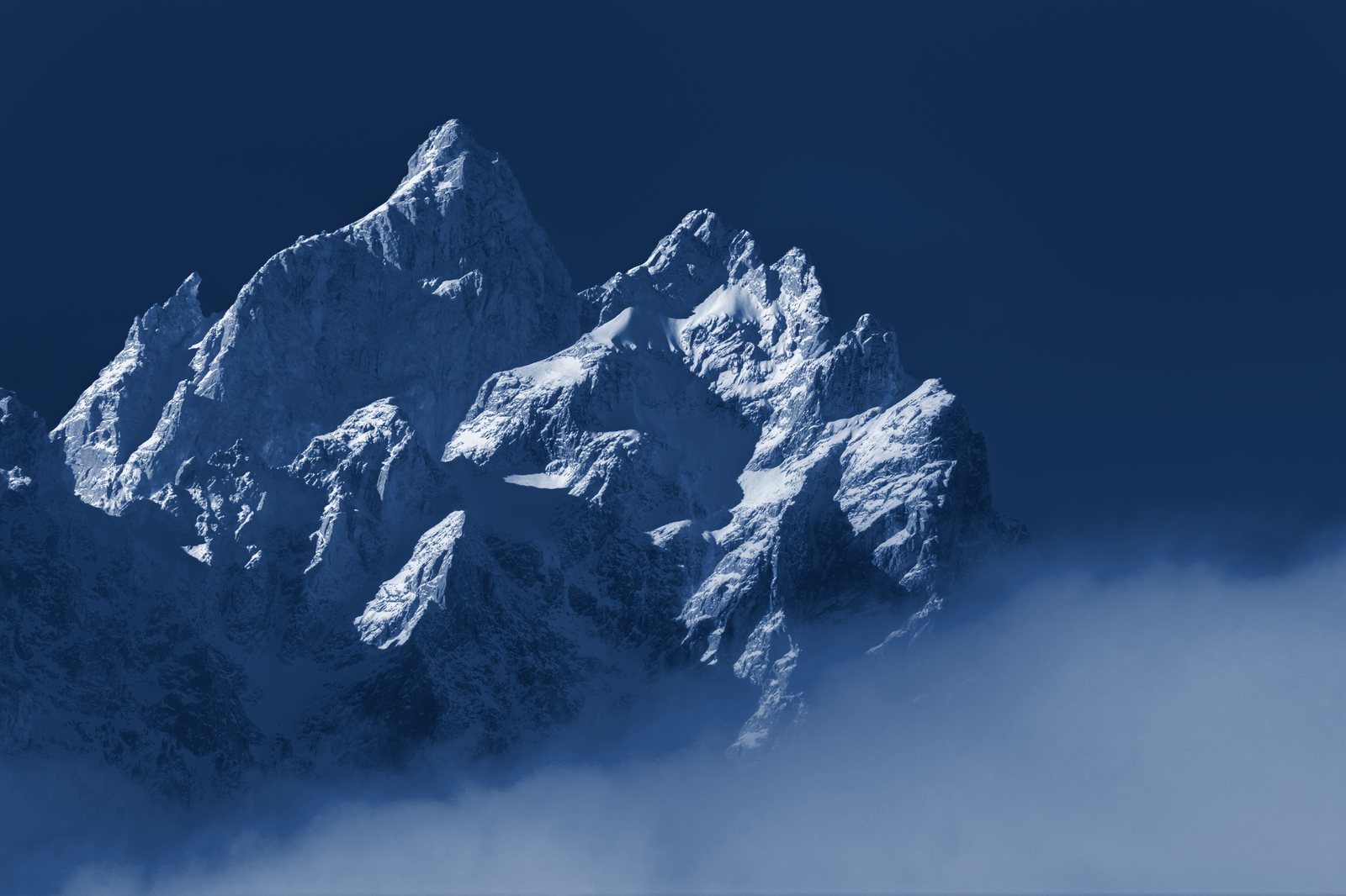 Snow-covered peaks of the Teton Range rising above a sea of cloud